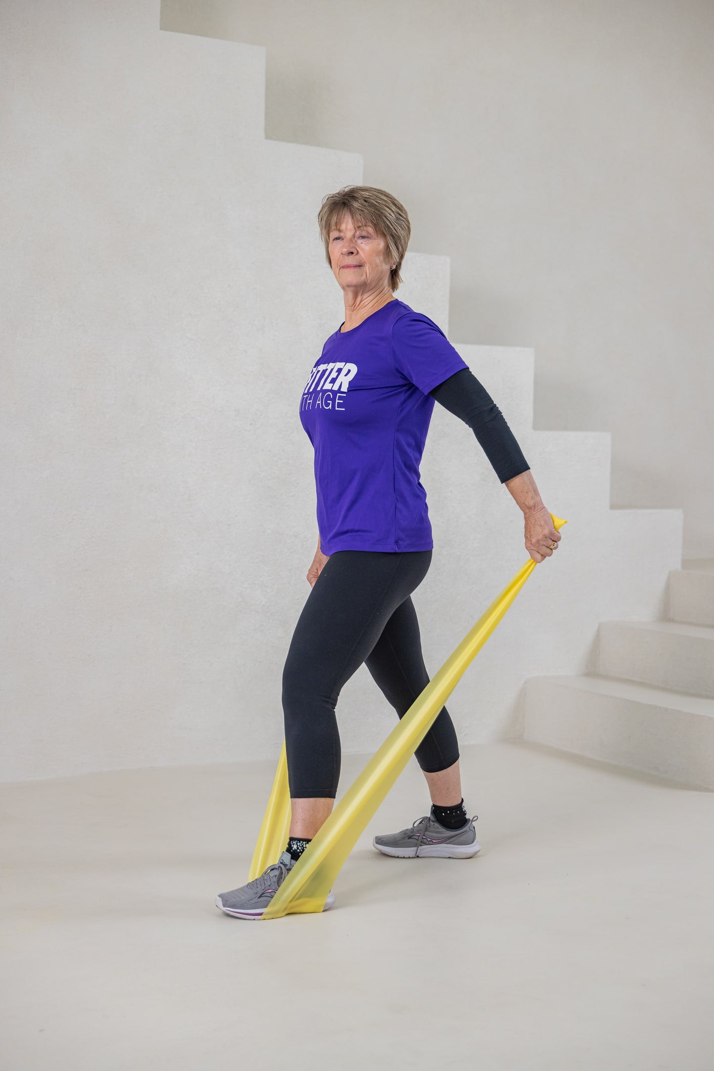 A women standing and using an exercise band that is yellow